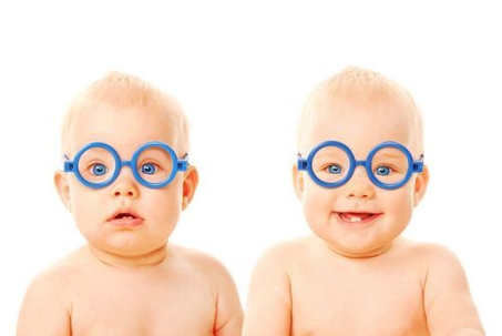 Two babies wearing glasses sitting next to each other.