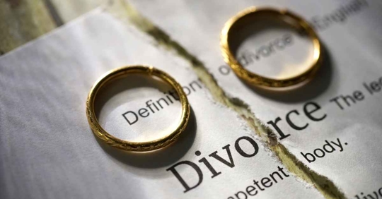 Two wedding rings sitting on top of a piece of paper with the definition of divorce written on it that's been ripped in half.