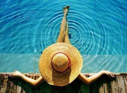 A person sitting in a swimming pool relaxing while wearing a sun hat.