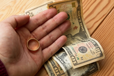 man's hand holding wedding ring on top of money