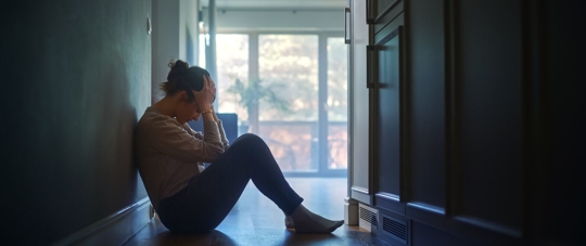 Sad Young Woman Sitting on the Floor In the Hallway of Her Appartment, Covering Face with Hands.
