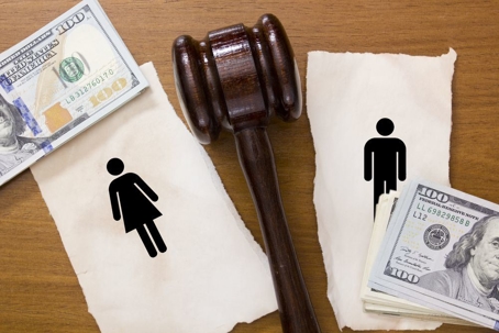 A judge's gavel sitting on a table between a male sign and a female sign that each have money stacked on them.