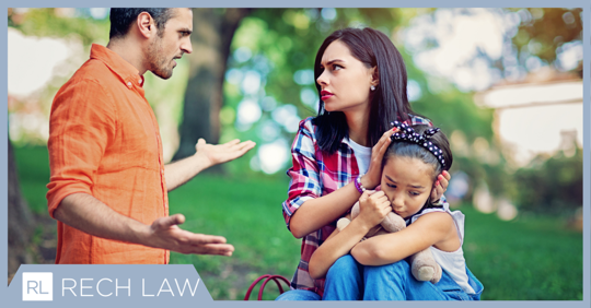 A mother holding her hands over her daughter's ears while she argues with the child's father.